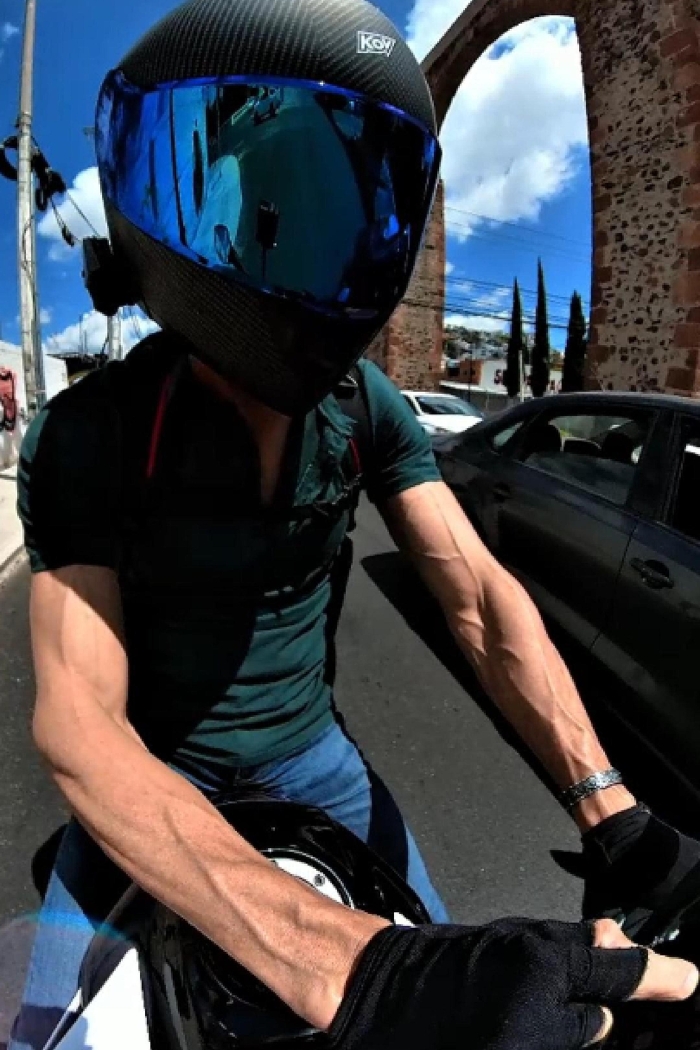 Eric at a stop while riding a motorcycle with hunter green short sleeve shirt and full black helmet alongside the aqueduct in Querétaro, QRO, Mexico.